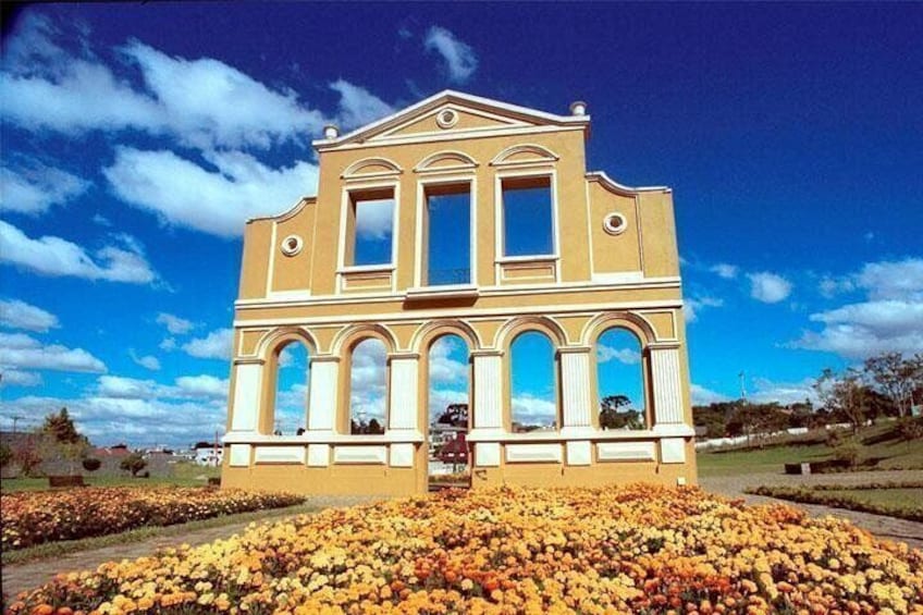 A building with a yellow facade and white arches, surrounded by a field of flowers. 2