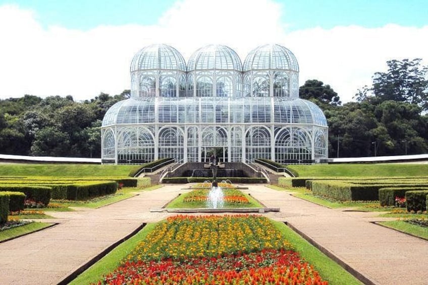 A glass conservatory with a fountain in the center, surrounded by well-manicured gardens. 2