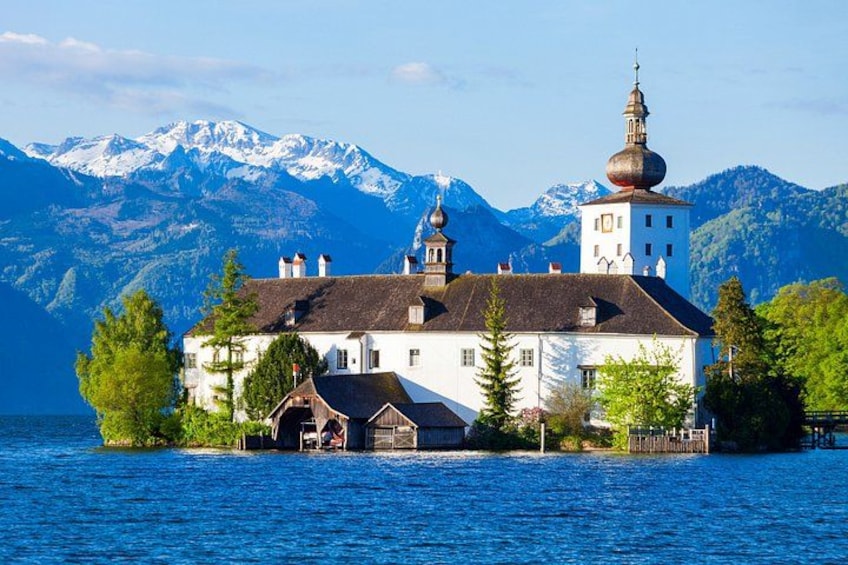 A lakeside building with a bell tower, surrounded by mountains and trees. 3