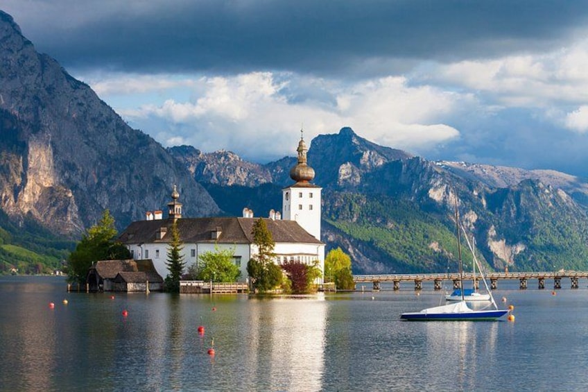 A lake with a white church, a bridge, and mountains in the background. 2