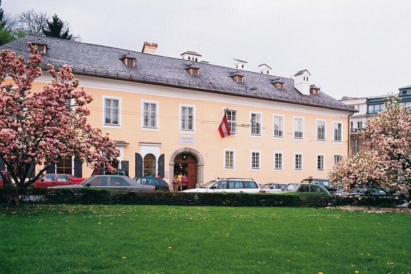 A building with a yellow facade, parked cars, and blooming trees. 2