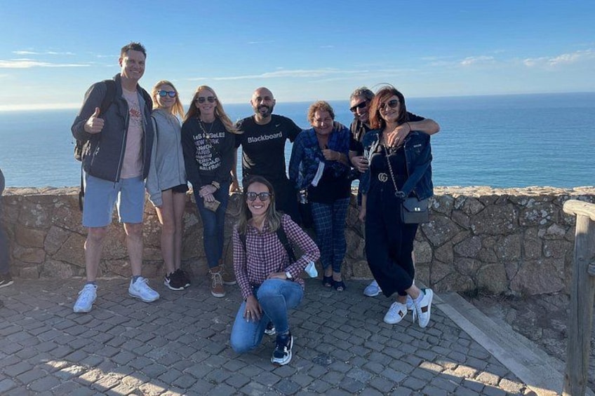 A group of people posing on a stone wall overlooking the ocean. 2