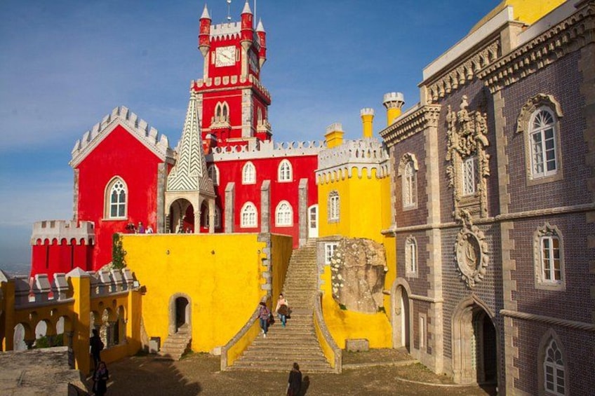 A colorful castle with red and yellow walls, a clock tower, and a staircase leading to the entrance. 2