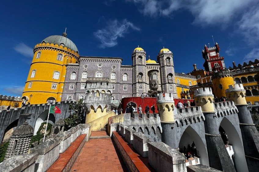 A historic castle with yellow and grey towers, a red brick pathway, and a clear blue sky. 3