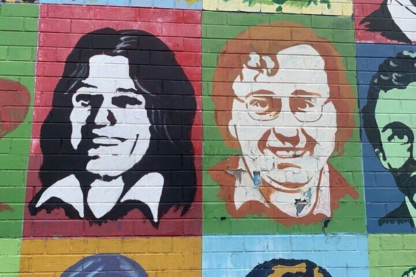 A colorful mural with various portraits on a brick wall. 5