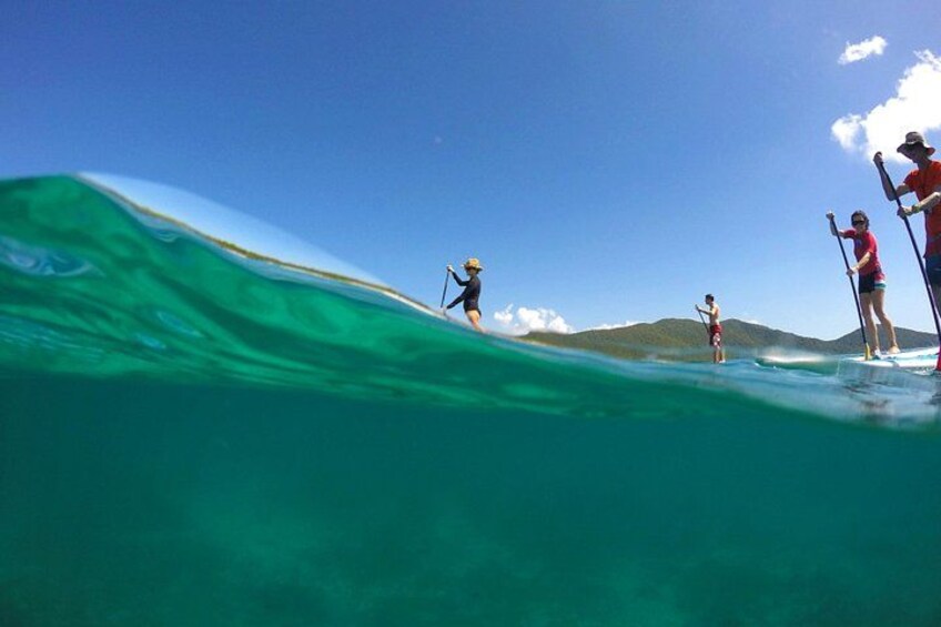 Des personnes pratiquent le paddle sur une eau turquoise, sous un ciel dégagé, avec des montagnes qui se dessinent à l’horizon. 5