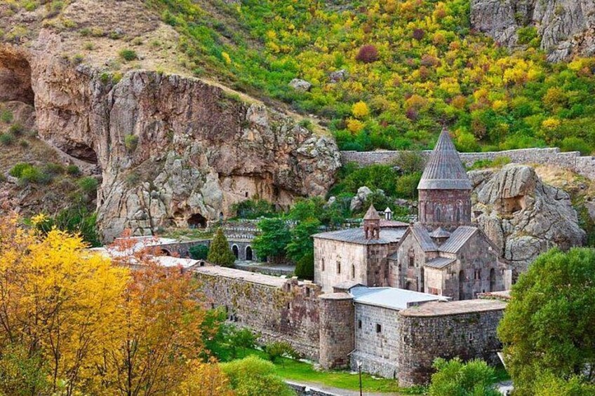 Una iglesia de piedra histórica con un campanario, rodeada de exuberante vegetación y terreno rocoso. 2