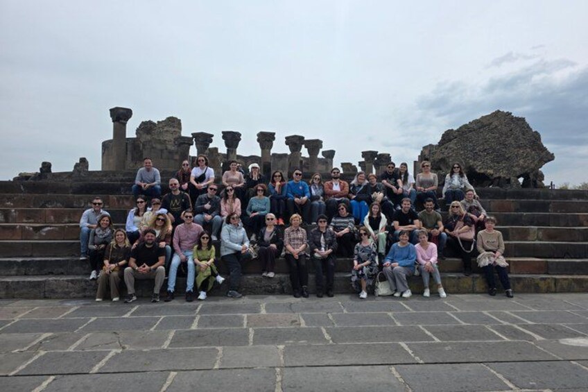 Un grupo de personas posando frente a unas ruinas antiguas con columnas y una gran estructura de piedra. 5