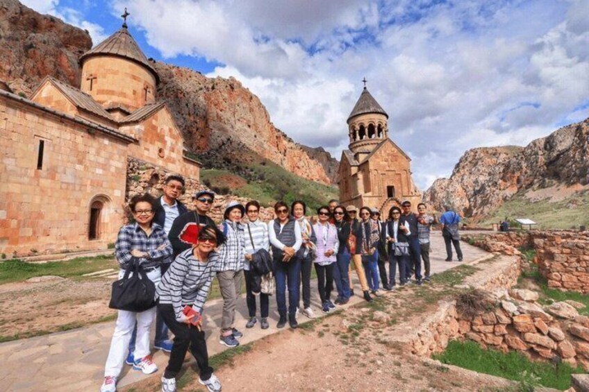 A group of people standing in front of a church with two domed towers, surrounded by rocky terrain. 1