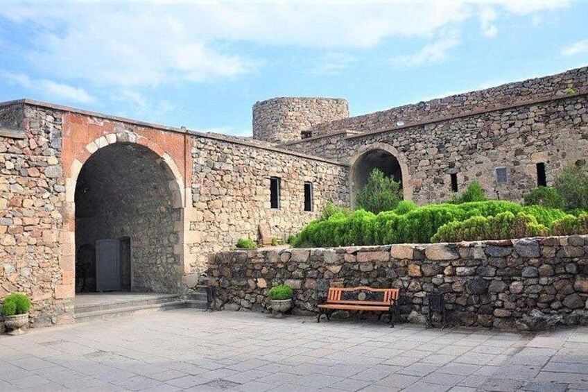 Ein Gebäude aus Stein mit Rundbögen, einer Bank und einer Steinmauer mit Pflanzenbewuchs. 2