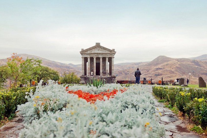 A neoclassical building with columns, surrounded by a garden with white and red flowers, and mountains in the background. 4