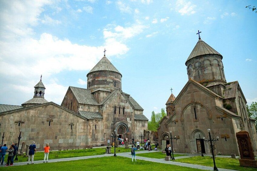 A historic church with multiple domes and crosses, surrounded by a green lawn and a few people. 2