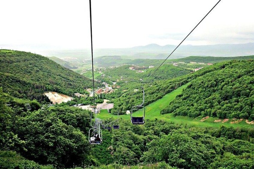 Un sistema de teleférico en una zona montañosa con abundante vegetación y edificios a lo lejos. 3