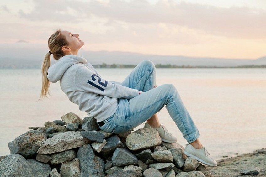 Una persona sentada sobre rocas junto a un cuerpo de agua al atardecer. 4
