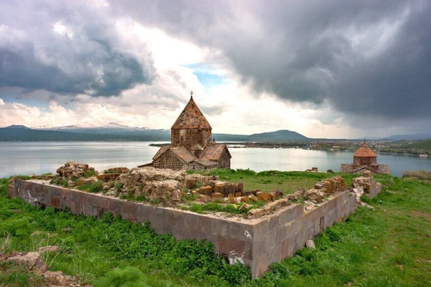Ruinas antiguas con una iglesia y un campanario junto a un lago, con montañas al fondo. 2