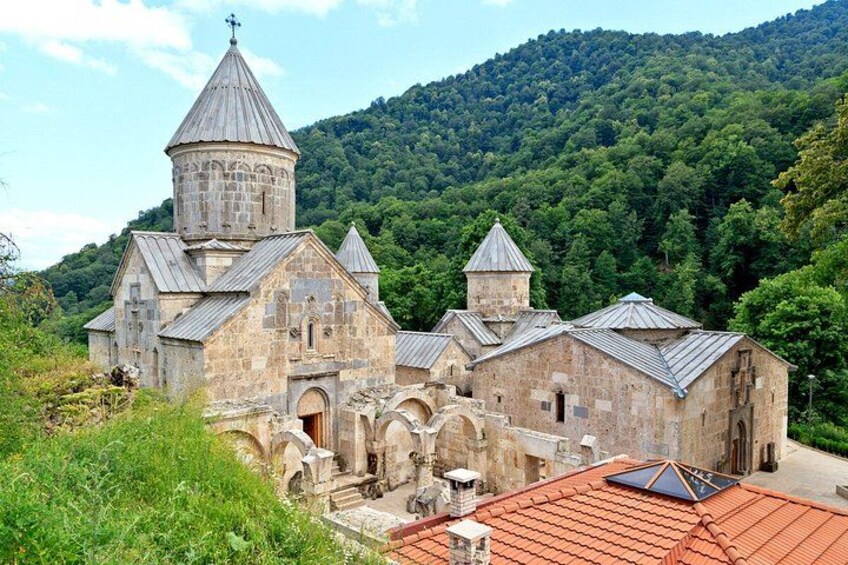 A stone church with a bell tower, surrounded by lush greenery and hills. 1