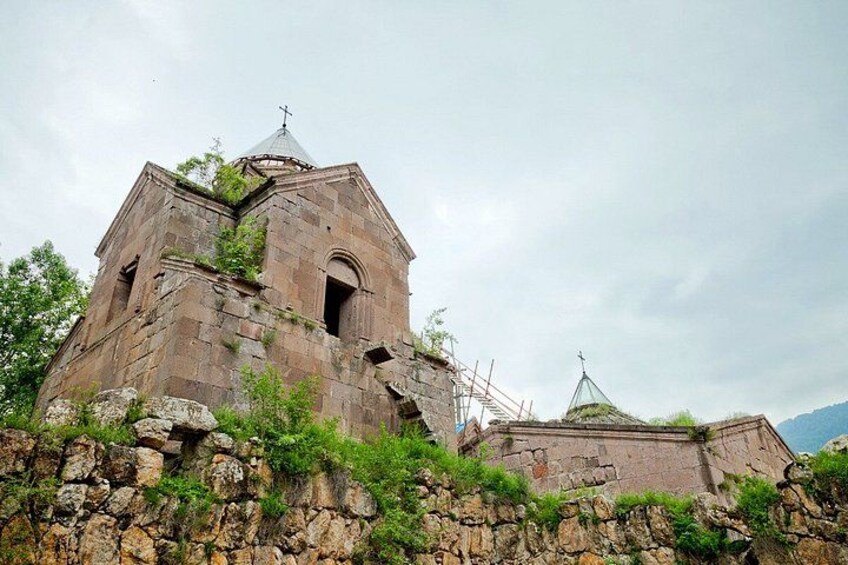 A stone church with a bell tower, surrounded by greenery and a stone wall. 3
