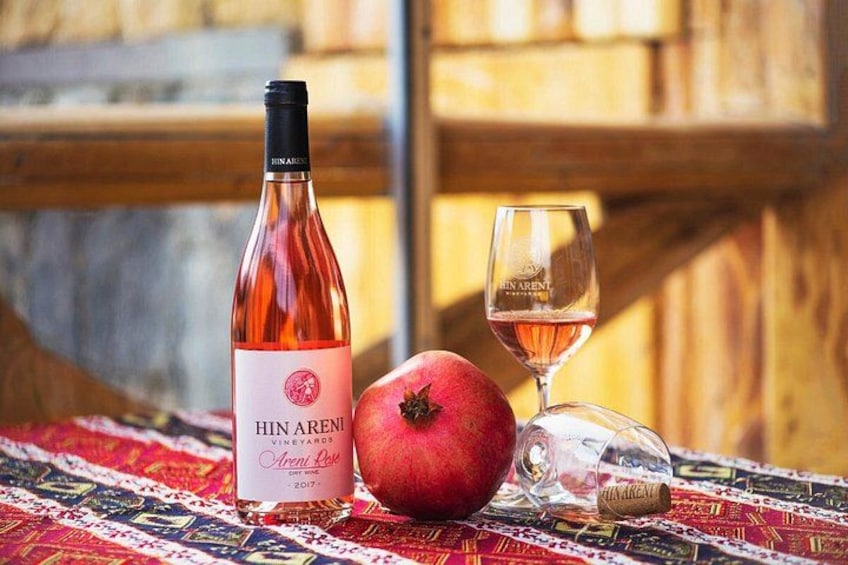 Una botella de vino Hinaren, una copa de vino y una granada sobre un mantel estampado. 2