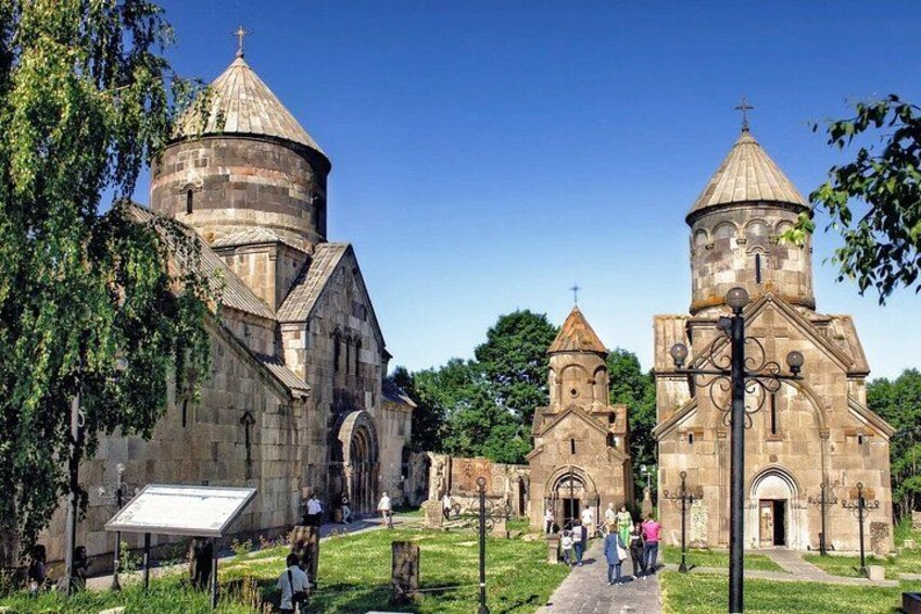 Eine historische Kirche mit mehreren Kuppeln und einem Glockenturm, umgeben von Grünflächen und wolkenlosem Himmel. 2