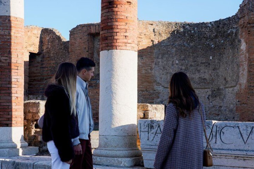 A group of people standing near ancient ruins with columns and inscriptions. 1