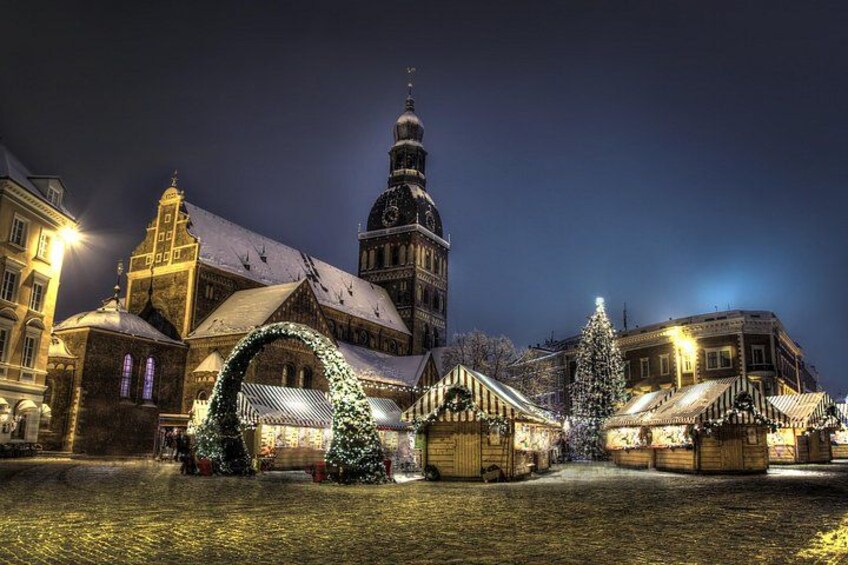 Une place historique illuminée la nuit, avec des bâtiments éclairés, un clocher d’église imposant et des décorations de Noël. 3