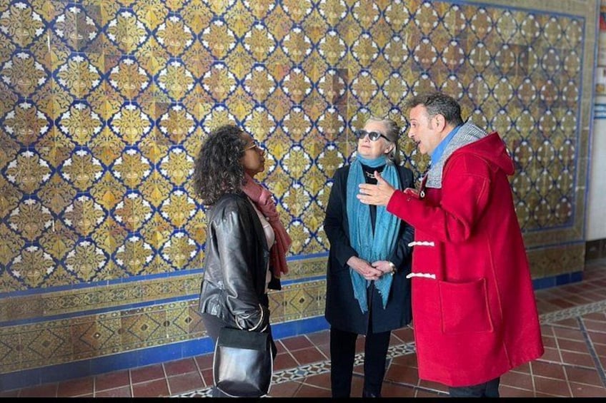 Un mur orné de motifs, une personne portant un manteau rouge et deux autres individus. 3