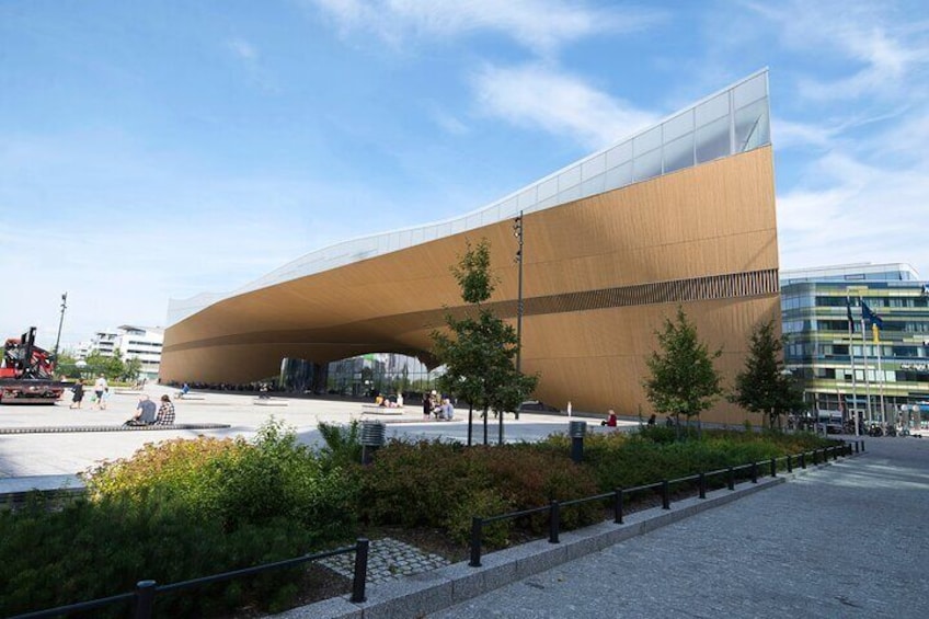 En moderne bygning med arkitektonisk design og en buet facade, omgivet af en anlagt have med træer og en belagt sti. 4