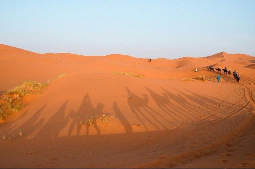 A desert landscape with sand dunes and a group of people riding camels. 3
