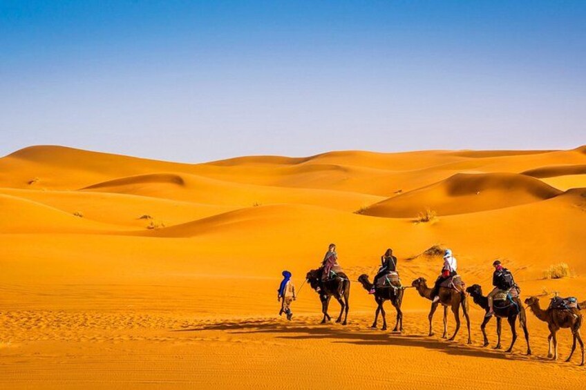 A group of people riding camels across a desert landscape with sand dunes. 2