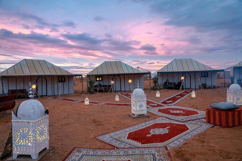A desert campsite with tents, lanterns, and patterned rugs. 3