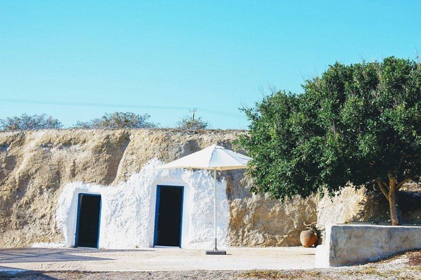 A white building with two doors and a small roof, set against a hillside with sparse vegetation. 2