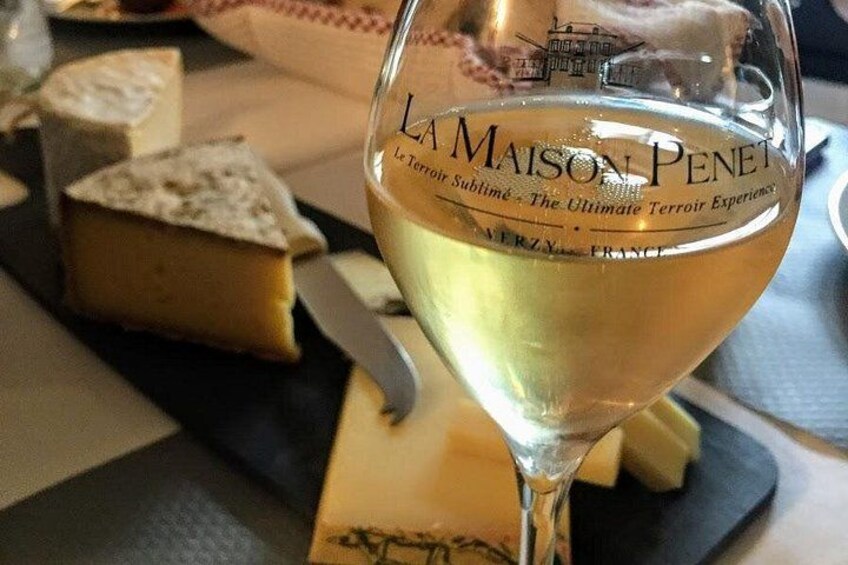 Una copa de vino blanco con una etiqueta que dice 'La Maison Penet' y un trozo de queso sobre un plato negro. 2