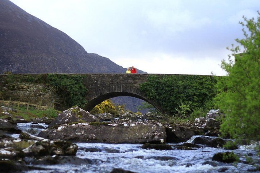 Un pont de pierre enjambe une rivière où l’on aperçoit une personne vêtue de rouge. 4