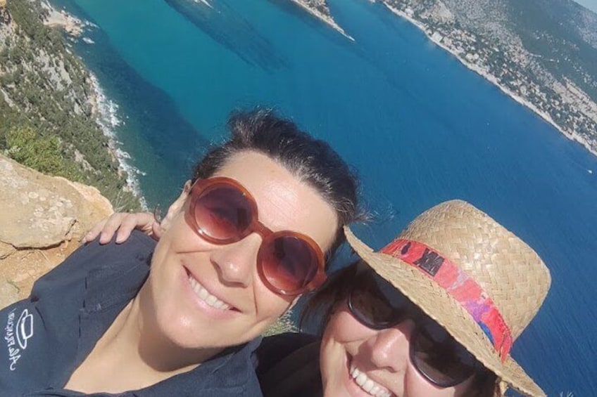 A person wearing a straw hat and sunglasses, overlooking a coastal landscape with clear blue waters and rocky terrain. 1