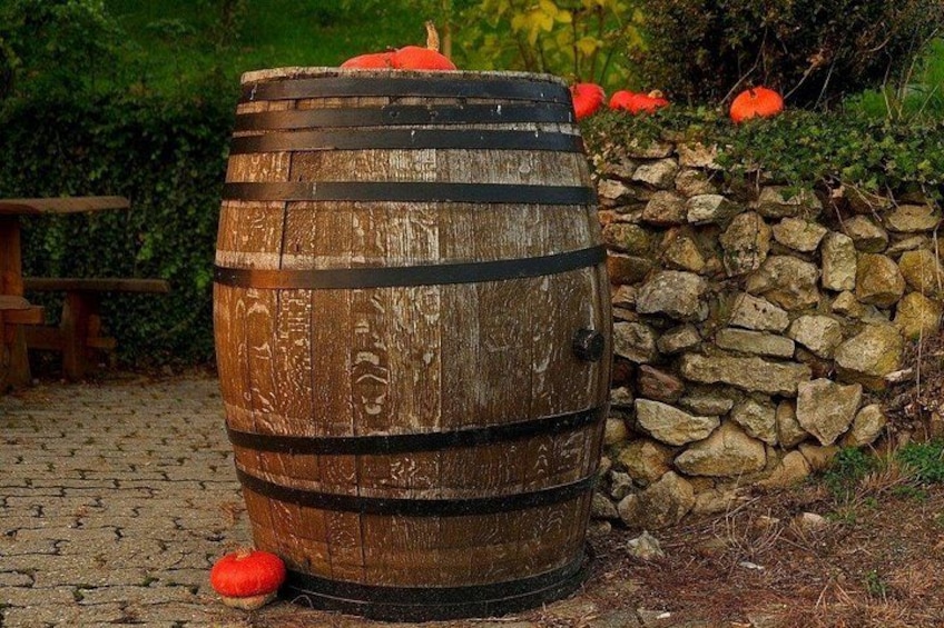 Een houten vat met metalen banden, buiten geplaatst in de buurt van een stenen muur en pompoenen. 2