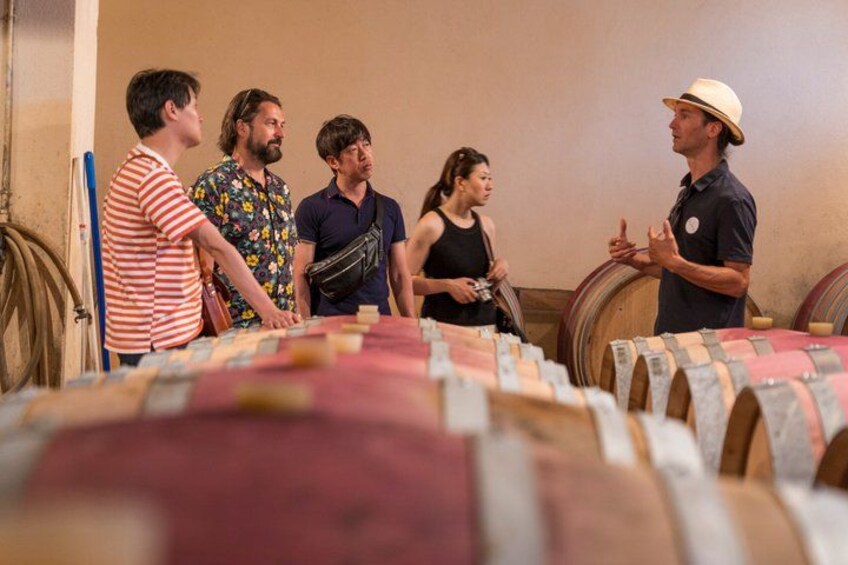 Un groupe de personnes se trouve dans une cave à vin, entouré de barriques en bois. 3