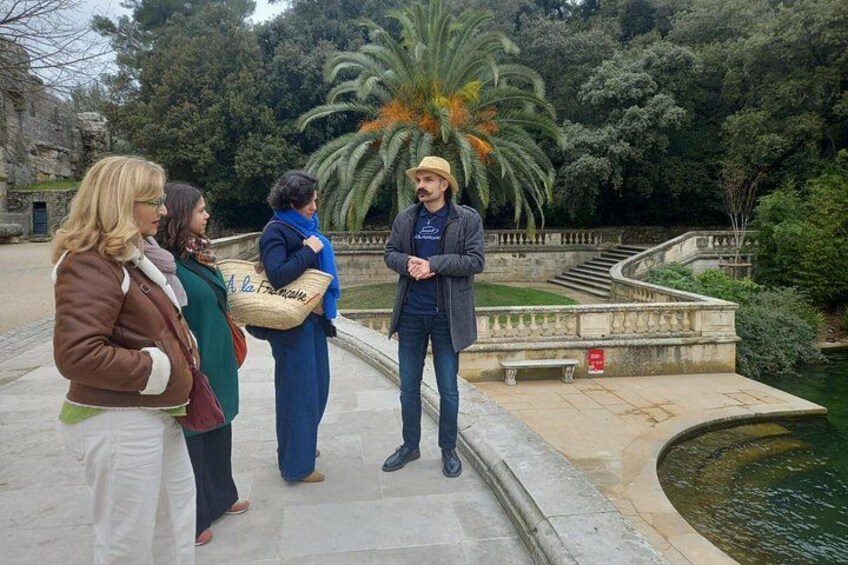 A group of people standing by a fountain in a park with a palm tree and stone architecture in the background. 3