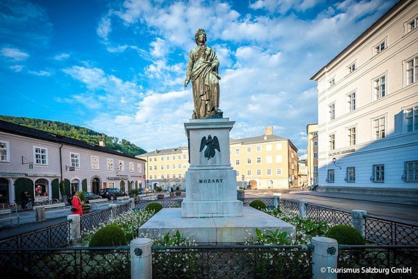 Eine Statue eines Mannes in historischer Umgebung, im Hintergrund Gebäude. 3