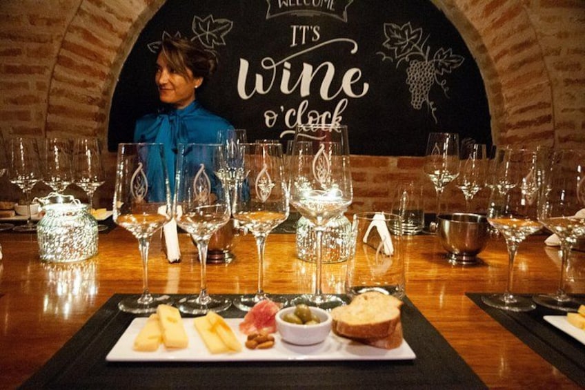 A wine tasting setup with glasses, a woman in the background, and a sign that reads 'It's Wine o'clock'. 1