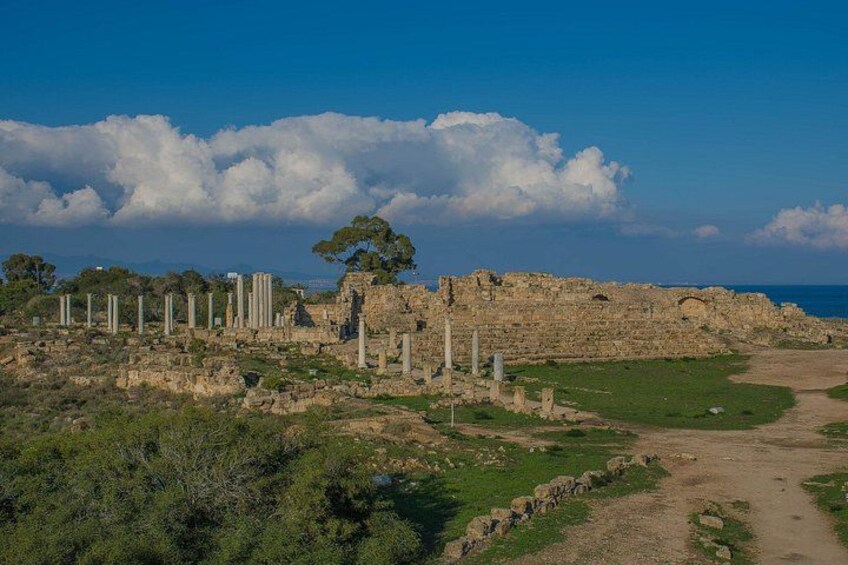 Ancient ruins with columns, a path, and a coastal backdrop. 2