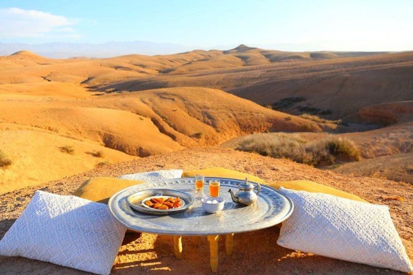 A picnic setup on a sandy dune with a table, plates, and a teapot. 3