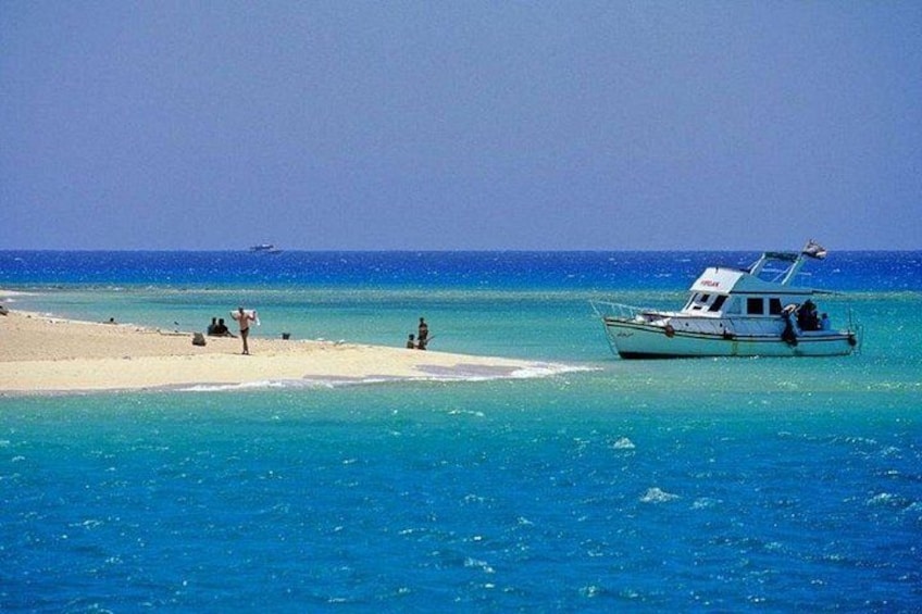 Una playa con agua turquesa cristalina, un bote pequeño y algunas personas en la orilla. 4