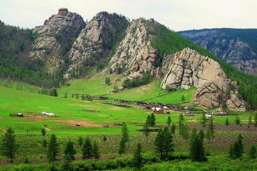 Un paisaje montañoso con afloramientos rocosos, campos verdes y edificios dispersos. 2