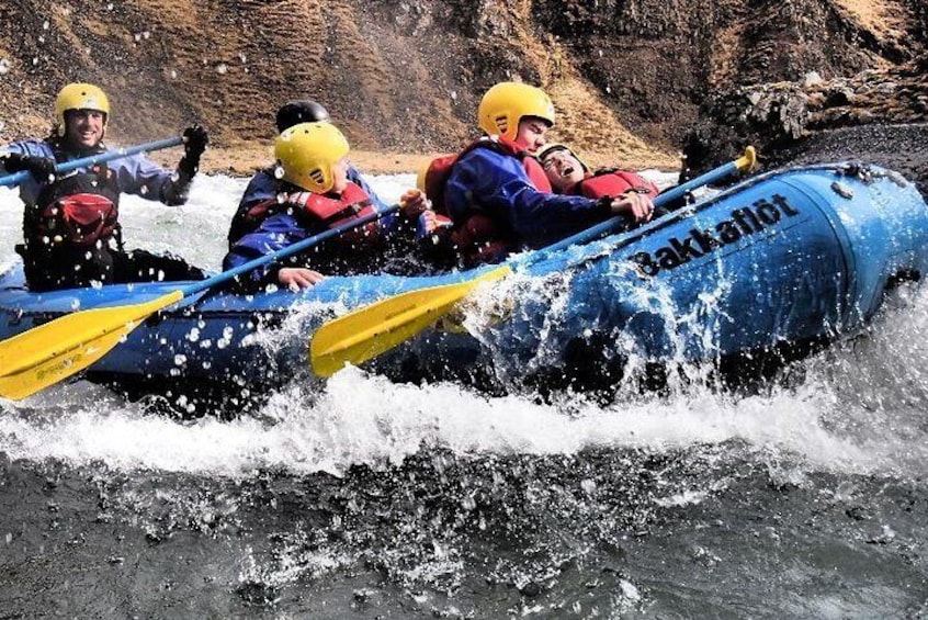 A group of people in a blue inflatable raft navigating a river with rapids. 1