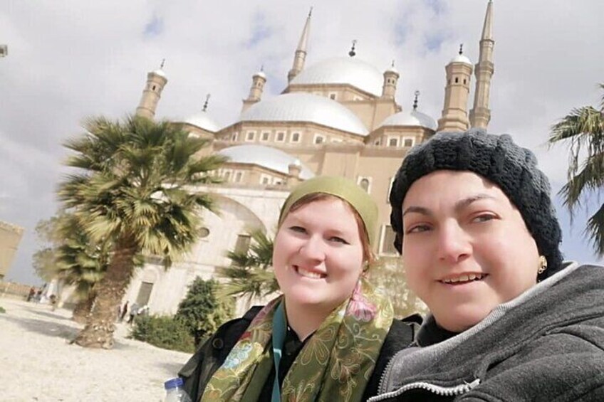 Two people in front of a large mosque with domes and minarets. 1