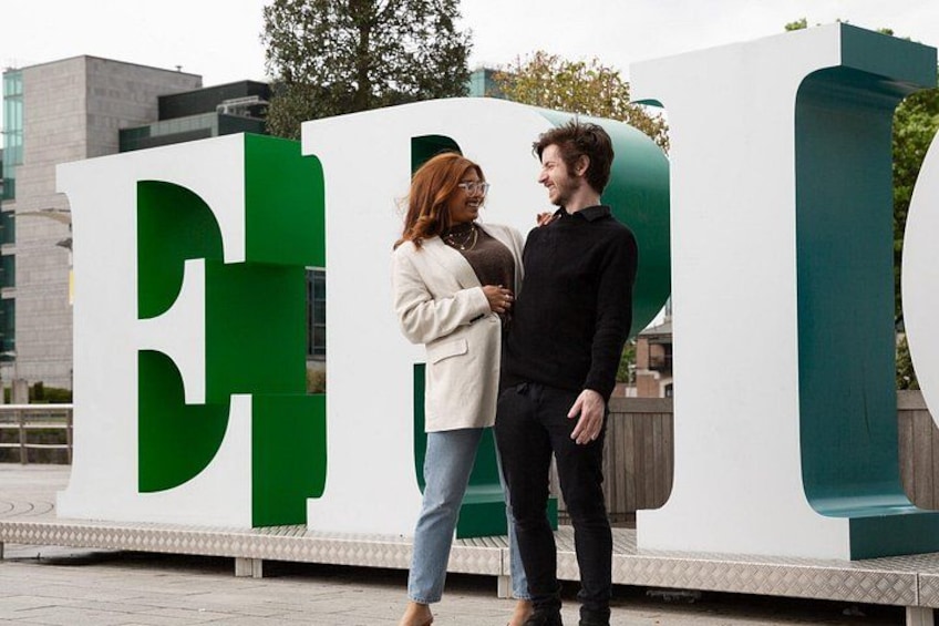To personer står foran en stor hvid og grøn bygning, hvor bogstaverne 'E' og 'P' er synlige. 2