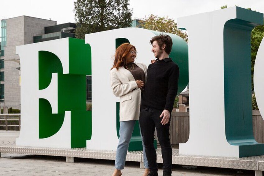 Due persone in piedi di fronte a un grande cartello bianco e verde con le lettere 'CH' ben visibili. 5