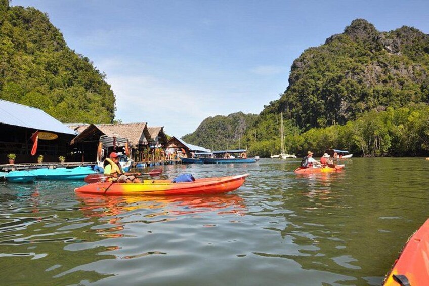 A calm river with kayaks, a thatched-roof building, and lush green hills. 3