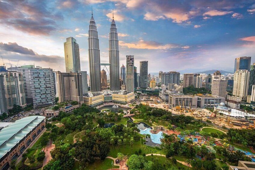 A cityscape with two prominent skyscrapers, a park with a water feature, and surrounding modern buildings. 5