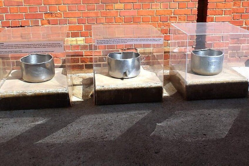Three metal pots on display in a transparent case against a brick wall. 1